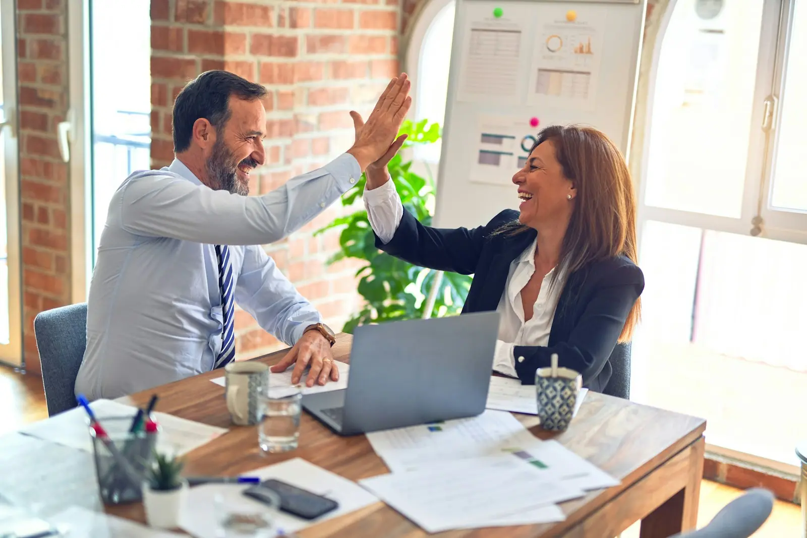 Two colleagues high-five over a laptop in a bright office